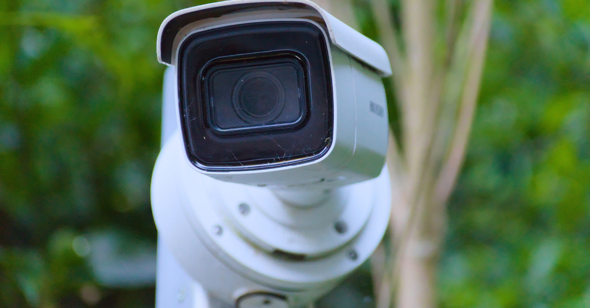Close-up of a white outdoor surveillance camera mounted on a pole, with a blurred green background.